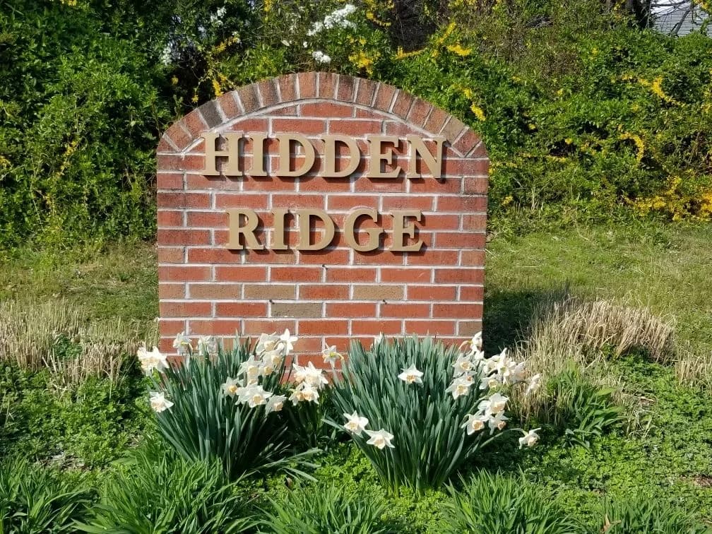 The brick Hidden Ridge sign with daffodils in front